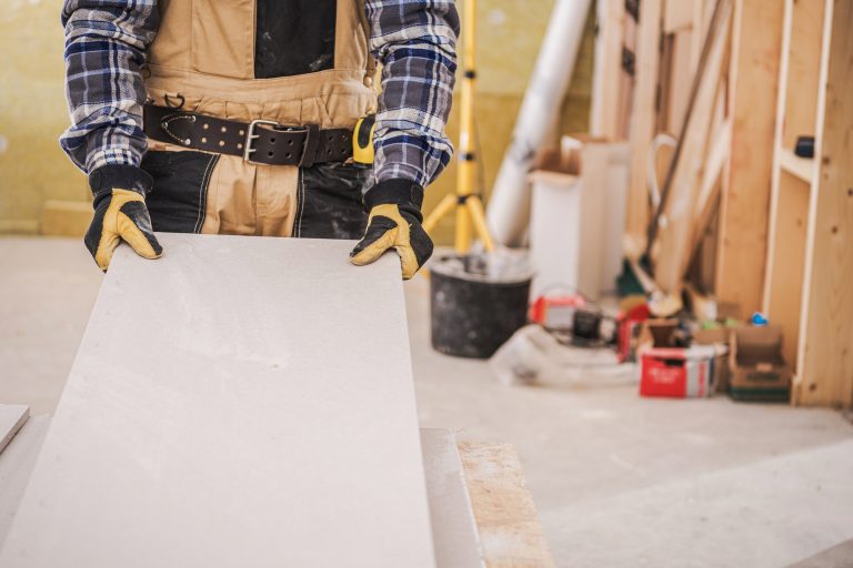 Male Contractor Holding Piece Of Drywall Material.